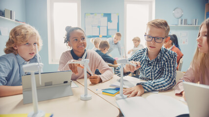Obraz premium In the Elementary School: Class of Smart Young Children Work as a Team Using Tablet Computers to Program Wind Turbines. Classroom with Kids Learning about Eco-Friendly Forms of Renewable Energy