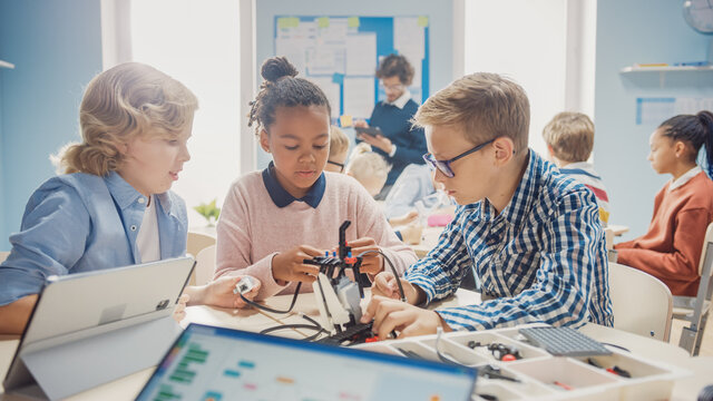 Elementary School Robotics Classroom: Diverse Group of Brilliant Children with Enthusiastic Teacher Building and Programming Robot. Kids Learning Software Design and Creative Robotics Engineering