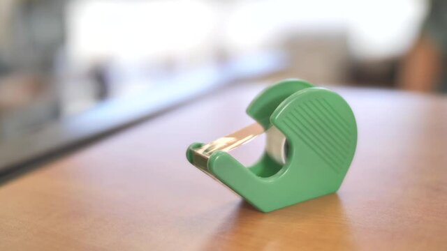 Hand take strip of adhesive tape from plastic dispenser, office workspace