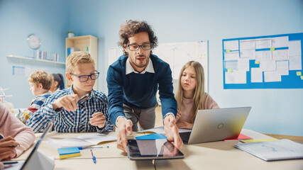 Elementary School Classroom: Enthusiastic Teacher Holding Tablet Computer Explains Lesson to Brilliant Young Children. Kids Learning Programming Languages, Internet Safety and Information Technology