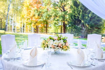 Wedding table with white tablecloth, outdoor setting, view of autumn bright yellow and orange trees