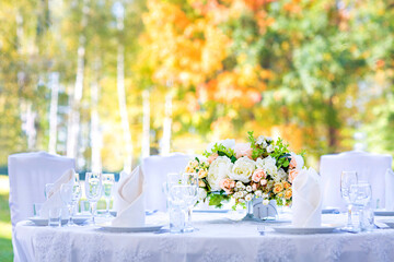 Wedding table with white tablecloth, outdoor setting, view of autumn bright yellow and orange trees