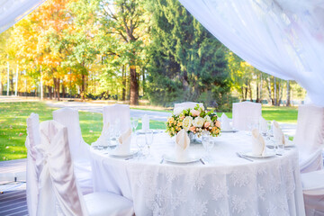Wedding table with white tablecloth, outdoor setting, view of autumn bright yellow and orange trees