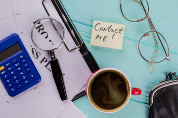 Sticky paper with Contact me word on blue office table. Cup of coffee papers glasses magnifier...