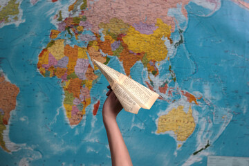 Fototapeta na wymiar symbol of unattainable impossibility limitation journeys. hand holding a paper airplane on the background of the world map. the inability of the limited ban on travel from coronavirus