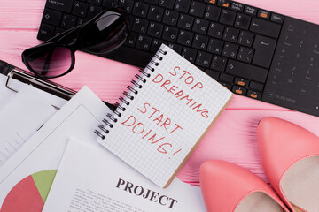 Close-up fashion woman accessories - sun glasses shoes on pink desk. Stop dreaming start doing on spiral notepad.