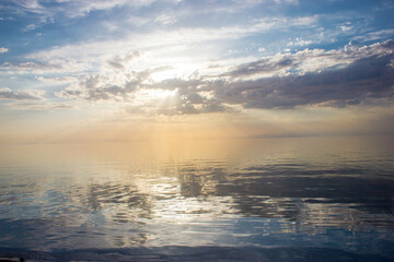 Colorful beautiful evening clouds above the water. Evening seacoast landscape with dusk, sun rays and ocean waves. Calm silver evening clouds on sky