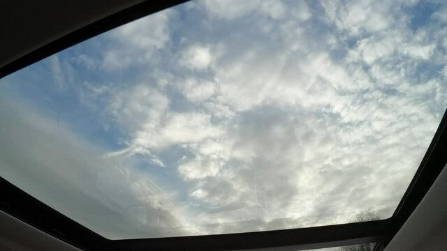 Panoramic glass sun roof in the car. View of the cloudy sky through the open hatch of the car.