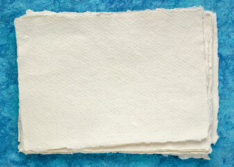 small sheet of blank white Khadi rag paper from South India against blue bark paper