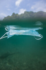Face mask floating in the ocean. Coronavirus protection becomes pollution. Ecology