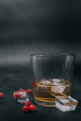 glass of whiskey with frozen berries and ice and smoke around