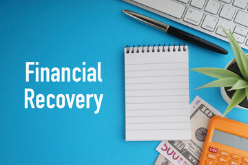 FINANCIAL RECOVERY text with banknotes currencies, fountain pen, notepad, decorative plant, keyboard and calculator on blue background. Coronavirus Covid19 and Business Concept
