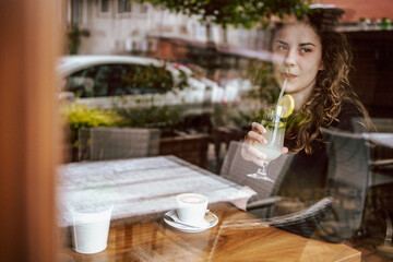 Cute brunette, curly girl sitting in a cafe, drinking coffee and juice.