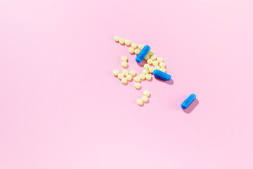 Yellow medicines with bare capsules on a pink background with hard shadows.