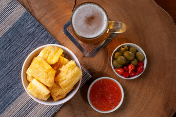 .Fried manioc. Traditional Brazilian food dish. Accompanied by pepper jam, olives and pepper pout. Glass of beer. Top view