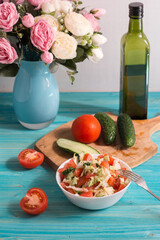 Cooking a vegetarian salad of fresh vegetables with olive oil on a blue wooden table. Light summer dinner. In the background, a bouquet of flowers