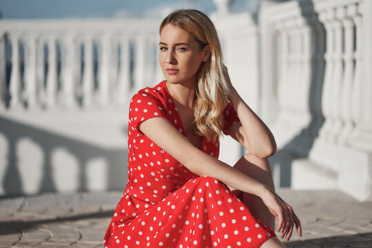 Blond young woman on red dress sitting on floor  