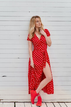 Blond young woman on red dress on beach and wooden background 