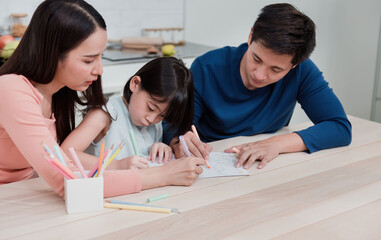 Asian women and men teaching girls to write and draw on paper. Three people had a happy facial expression at home It is a new way of life for the family.