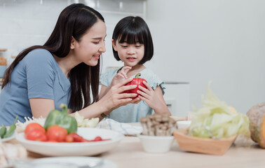 Beautiful woman And two lovely Asian girls are teaching cooking in the kitchen at home. Two people are happy. It's a new normal way of life.