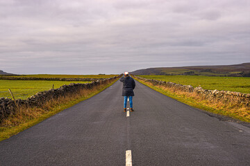 Photo of a man with a winter coat standing in the middle of the road surrounded by nature in the UK