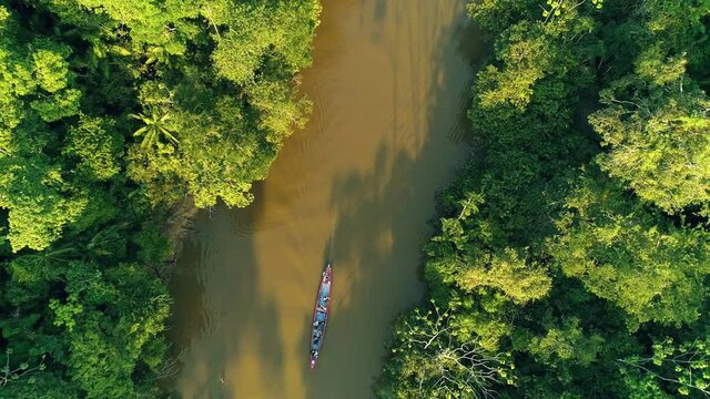Long Aerial Shot Moving Up Of A Boat Moving Along Brown Colored Amazon River With Lush Green Rainforest At Sunset Creating Shadows Of Trees In Cuyabeno Ecuador