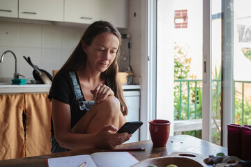 Natural woman with smart-phone sitting on wooden kitchen table