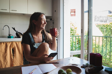 Natural woman with smart-phone sitting on wooden kitchen table