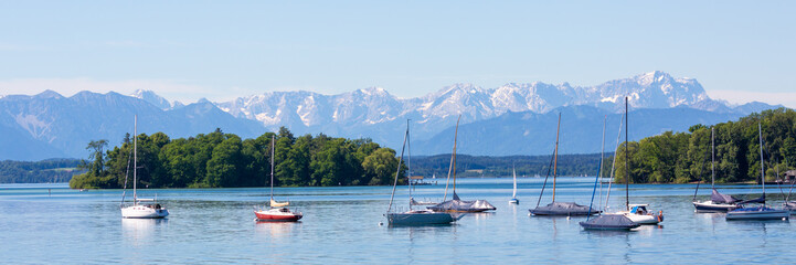 Panorama of Lake Starnberg with Roseninsel (rose island) and anchoring sailboats. Alps with Zugspitze at the horizon.