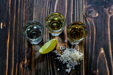 Mexican gold and silver tequila and lime salt on wood background