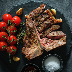 Sliced T-Bone Steak with salt, garlic, cherry tomatoes and pepper on  dark background.