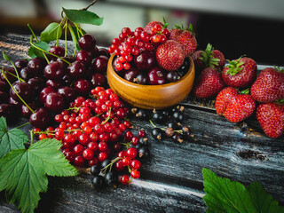 Ripe juicy red fruits and berries with green leaves on a wooden surface.