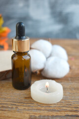 Close up aromatherapy composition with essential oil dropper, burning candle and cotton flower on wooden background. Spa. Cozy autumn or winter still life. Healthcare.