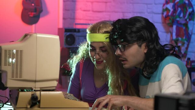 80s 90s boy and girl using a computer for the first time being impressed by what it can do. Funny vintage technology scene.