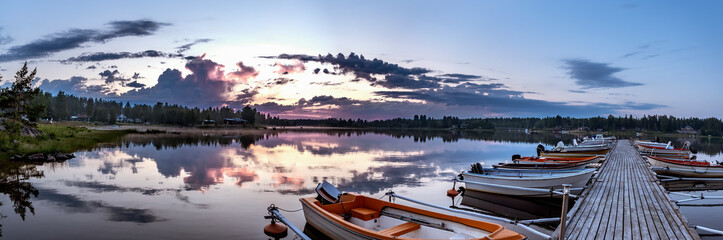 Sunrise during midnight light in Swedish Lapland, sea jetty, lot of parked boats, clouds reflection...