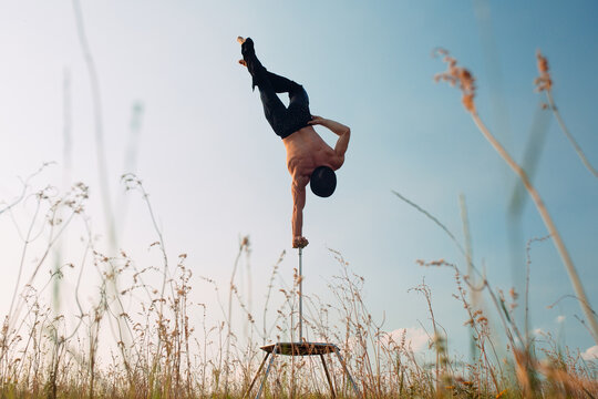 A man of athletic build performs complex gymnastic exercises in a field at sunset.