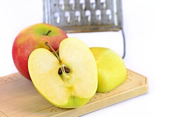 One red and one green sliced apple on a wooden board. Steel grater on apples in the background.