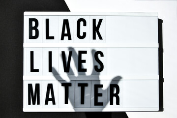 BLACK LIVES MATTER text with deep shadows of hand on a black and white background. Protest against...