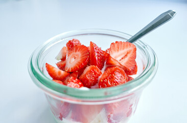 Red strawberry berries in a transparent cup with spoon, isolated on a white background. Vegetarian and healthy eating