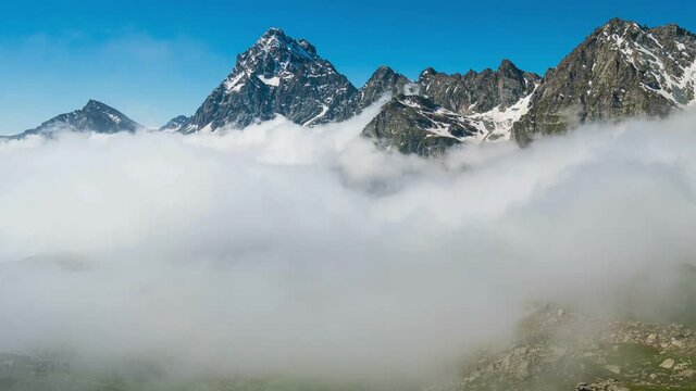 Time lapse, moving clouds in the valley below mountain ridges and peaks of the Alps. Majestic snow capped summit (M. Viso, 3841 m) against clear blue sky. Piedmont Italy