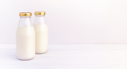 Two bottles of a fresh milk in a bottles with golden cap on a white table at morning, oatmeal, almond, alternative natural drink. Healthy organic beverage close-up on light background, copy space.