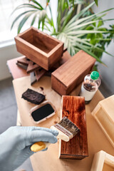 Man carpenter varnishing wooden crate for flowers with brush in her small business woodwork workshop. In your work, do you use stains or wood preservatives to show the wood pattern.