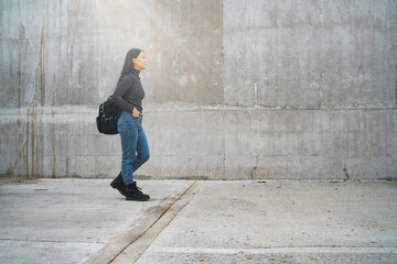 Asian woman walking against grey wall.