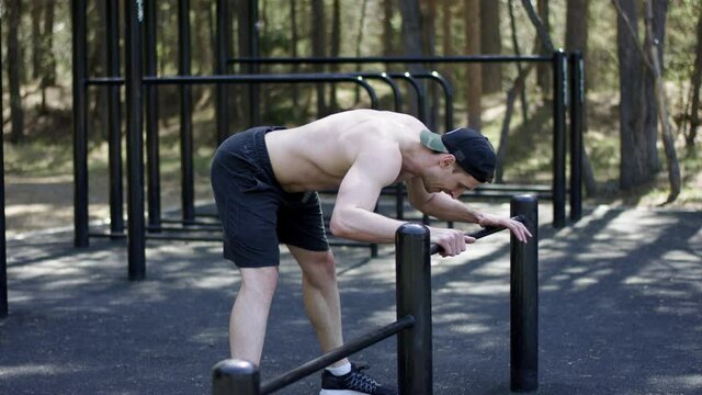 Adult caucasian attractive sportsman is doing an exercise for his legs at bars at the gym at the park during workout
