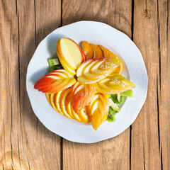 beautifully sliced fruit on a white plate, top view on a wooden table