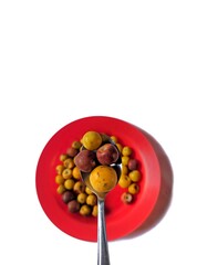 Yellow and brown nances on a red plate and a spoon with white background, typical fruit of Guatemala
