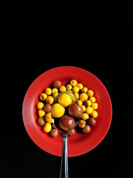 Yellow and brown nances on a red plate and a spoon with a black background, typical fruit of Guatemala