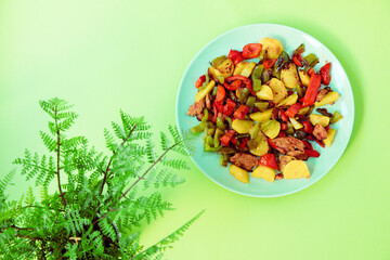 roasted potatoes with paprika in a green plate on a green background. french fries on a green background next to a plant as a decoration