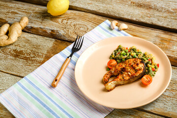 On a linen napkin is a plate with baked trout steak and quinoa with green vegetables and a fork next to it.