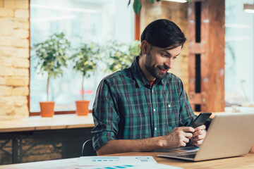 Mirthful man reading messages and smiling cheerfully